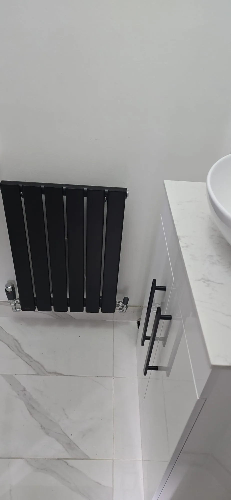 Matt black vertical designer radiator installed beside a marble-topped vanity unit in a Norfolk home