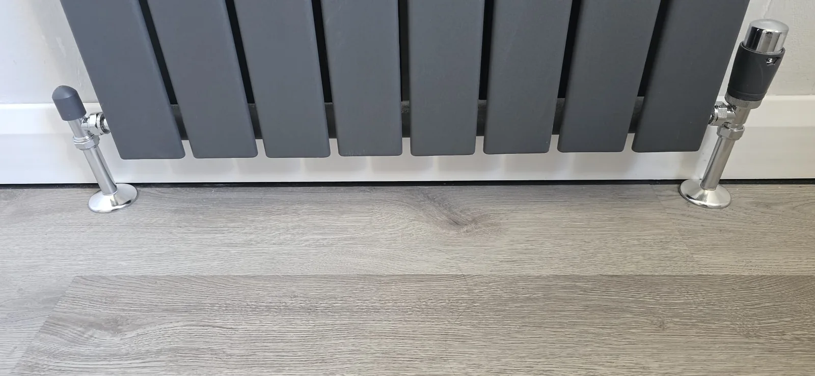 Anthracite grey designer column radiator fitted above wood-effect flooring during a central heating upgrade in Norfolk