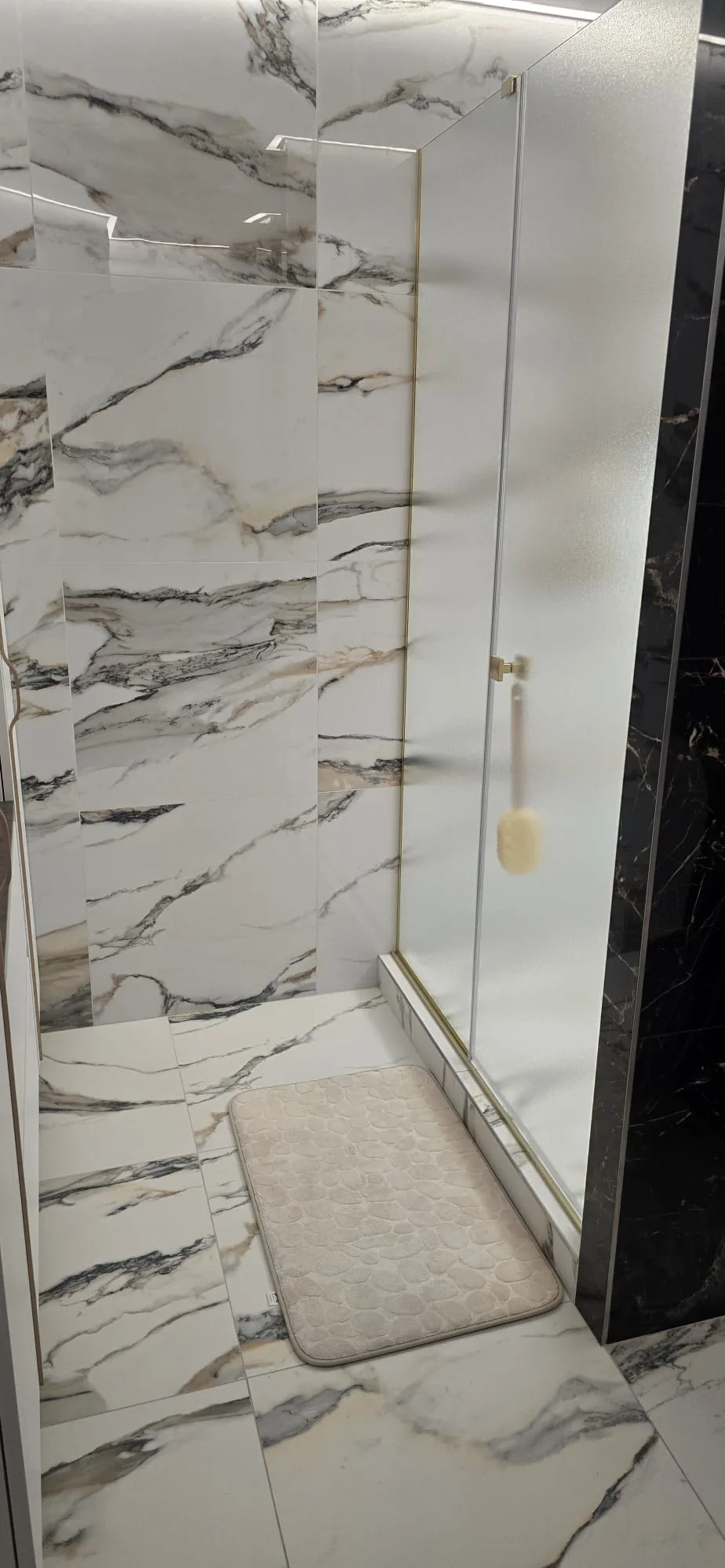 Walk-in shower enclosure with marble-effect tiles and a gold-framed glass screen installed in King's Lynn