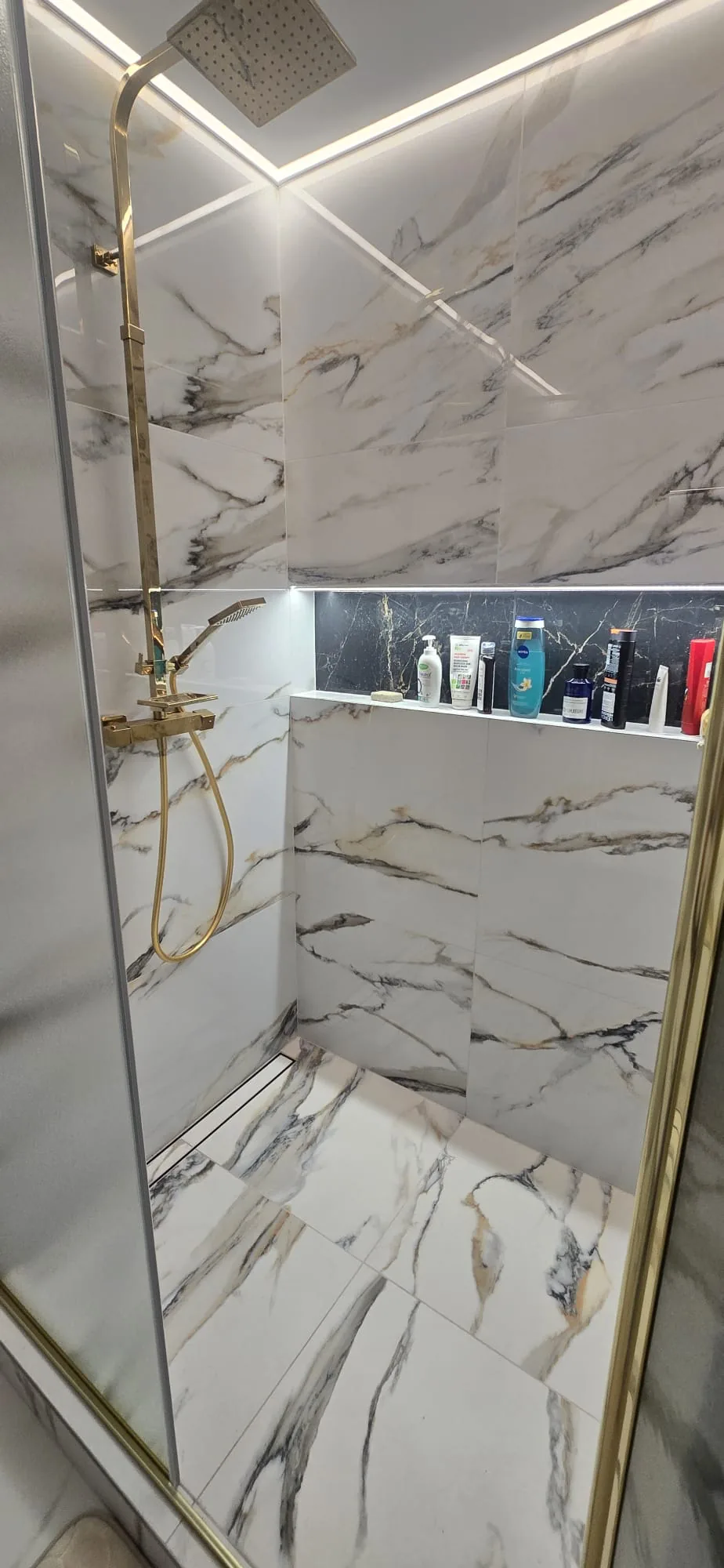 Brushed gold rainfall shower head and recessed shelf in a marble-tiled walk-in shower in King's Lynn