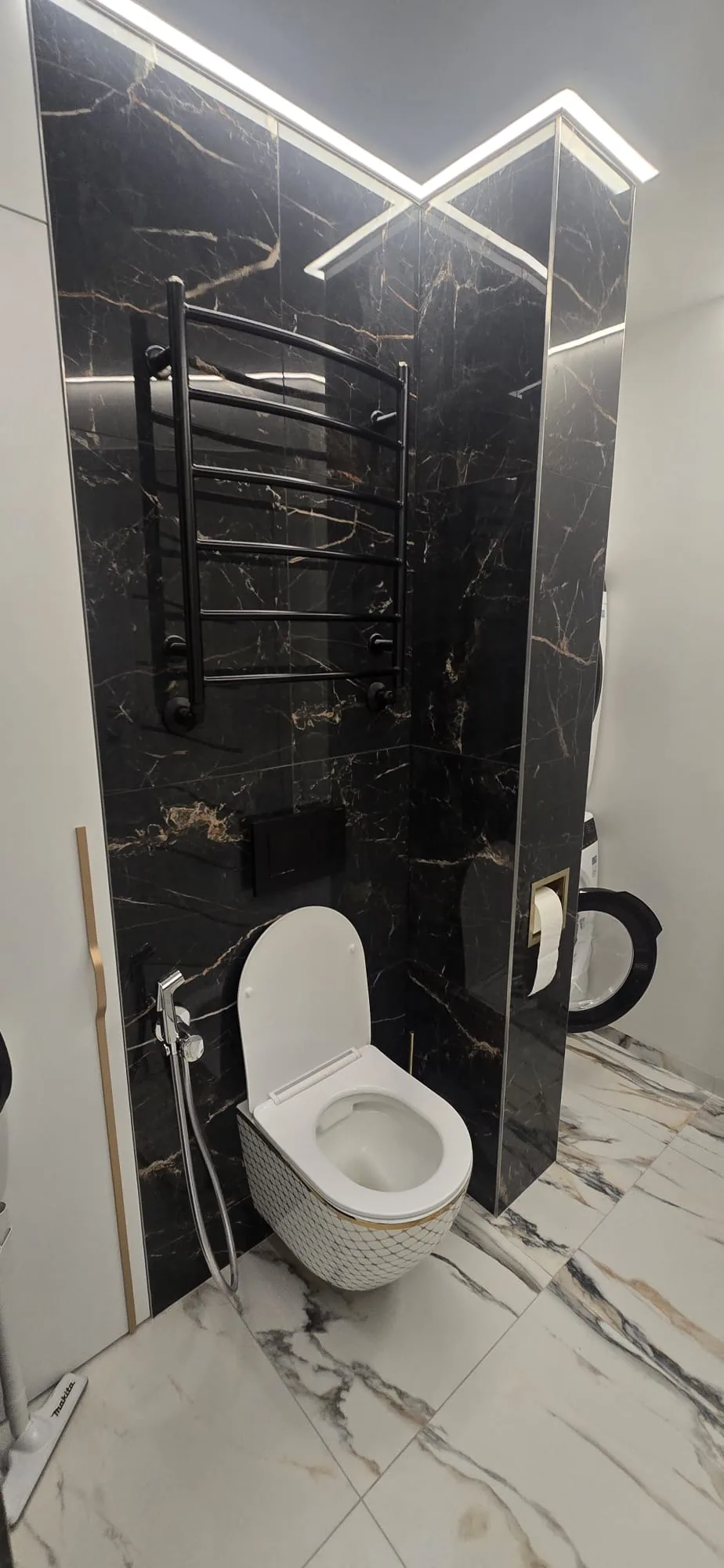 Wall-hung toilet and black heated towel rail against black marble-effect tiles in a King's Lynn bathroom