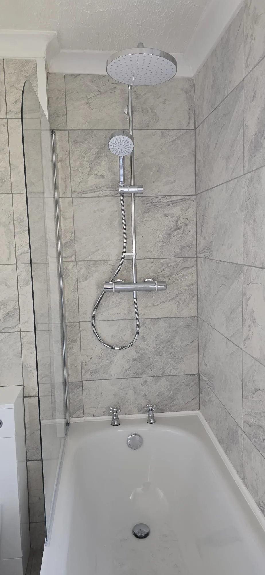 Chrome rainfall shower head over a white bath with grey marble tiling fitted in West Norfolk